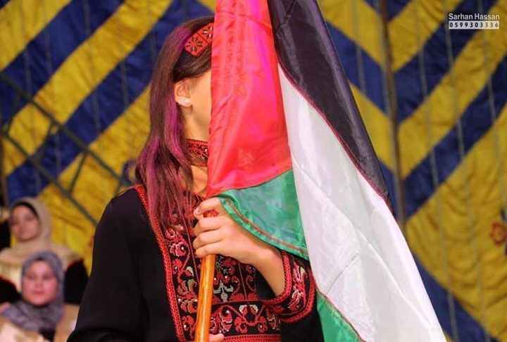 The child Salwa Shaath hides her tears behind the Palestinian flag after hearing the name of her martyr father during a ceremony held in Gaza Strip.