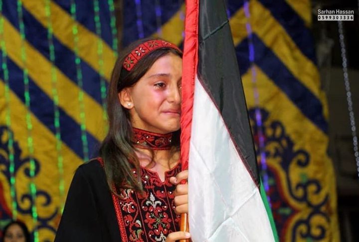 The child Salwa Shaath hides her tears behind the Palestinian flag after hearing the name of her martyr father during a ceremony held in Gaza Strip.